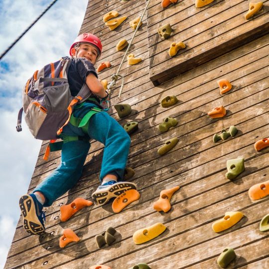 Boy on rock climbing wall with backpack