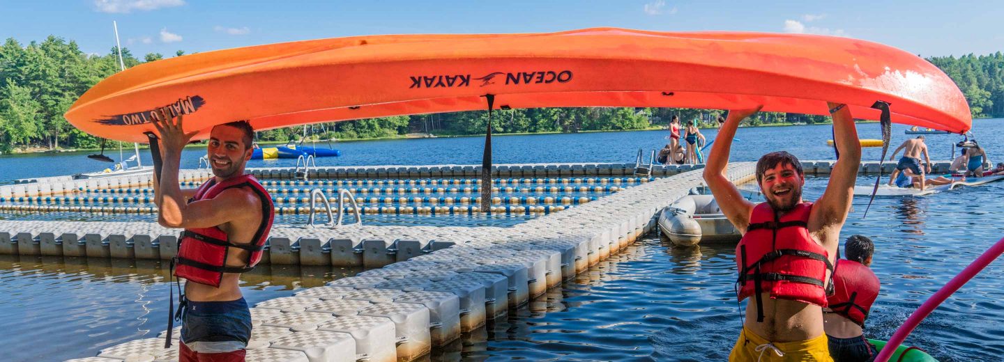 Staff carrying kayak by lake