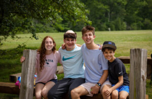4 students sitting together on a bench by a green meadow.