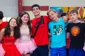 Group of students in costumes smiling together, arms around each other.